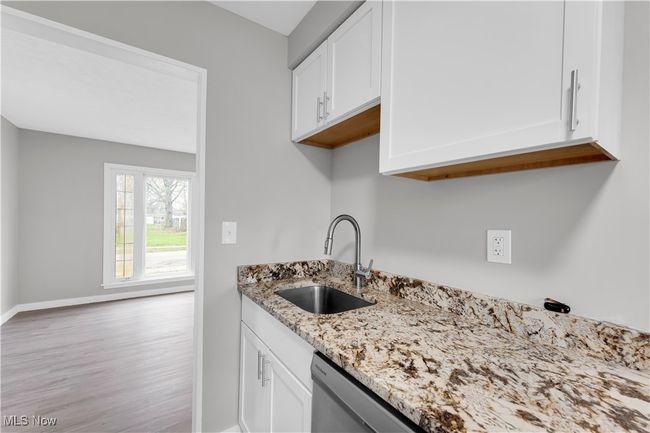 Kitchen with light stone counters, wood finished floors, white cabinets, and a sink | Image 11