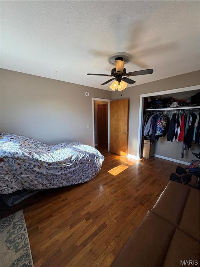 Bedroom with a textured ceiling, ceiling fan, a closet, and wood finished floors | Image 15