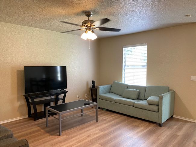 Living area featuring light wood-style floors, a textured wall, a ceiling fan, baseboards, and a textured ceiling | Image 4