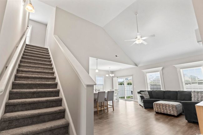 Living area with visible vents, stairs, wood finished floors, high vaulted ceiling, and ceiling fan with notable chandelier | Image 9
