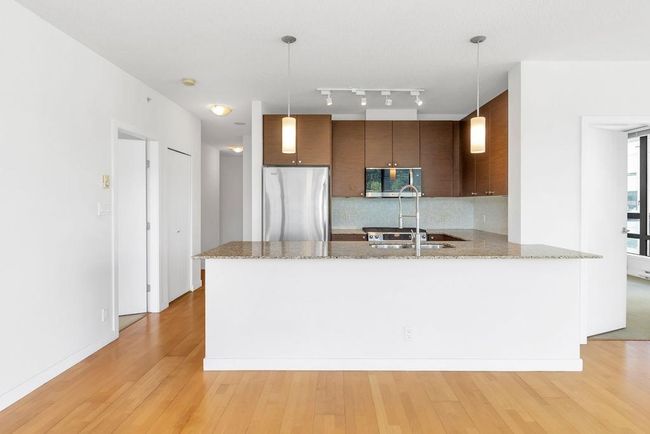 Kitchen featuring appliances with stainless steel finishes, light wood-type flooring, a peninsula, tasteful backsplash, and light stone countertops | Image 7