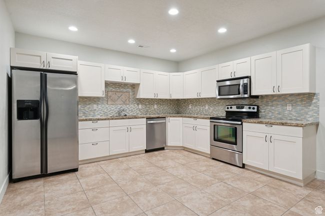 Kitchen with stainless steel appliances, a sink, backsplash, white cabinetry, and stone counters | Image 19