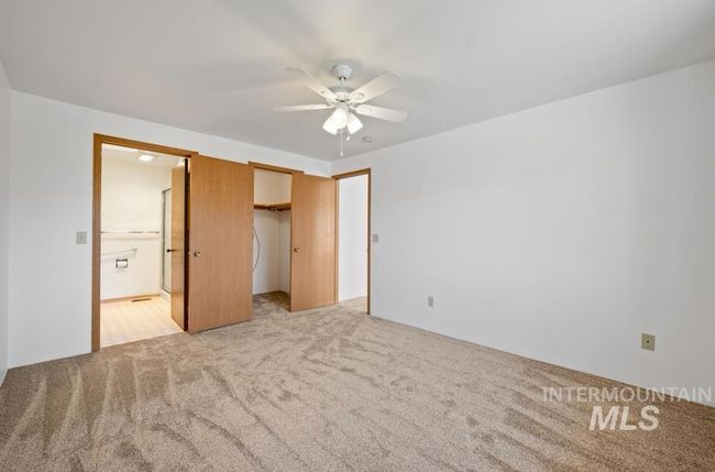 Unfurnished bedroom featuring light carpet, ensuite bath, a walk in closet, and a ceiling fan | Image 11