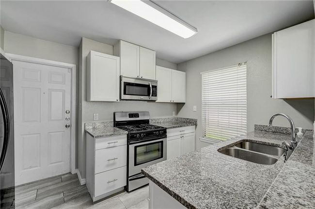 Kitchen featuring appliances with stainless steel finishes, a sink, white cabinetry, and light stone counters | Image 11