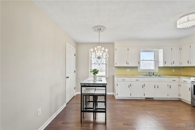Kitchen with dark wood-type flooring, white cabinets, a sink, and an inviting chandelier | Image 10
