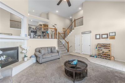 Living room with a high ceiling, a tiled fireplace, ceiling fan, and light colored carpet previously staged | Image 1