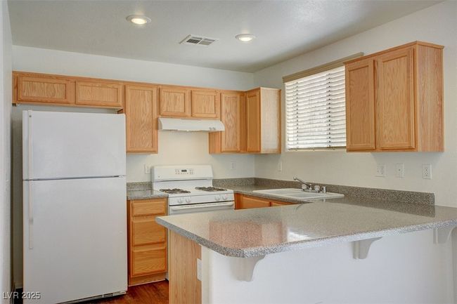 Kitchen featuring a sink, under cabinet range hood, visible vents, a peninsula, and white appliances | Image 9