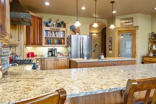 Kitchen featuring freestanding refrigerator, arched walkways, a sink, light stone countertops, and recessed lighting | Image 16