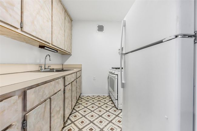 Kitchen featuring visible vents, light brown cabinetry, a sink, white appliances, and light countertops | Image 5