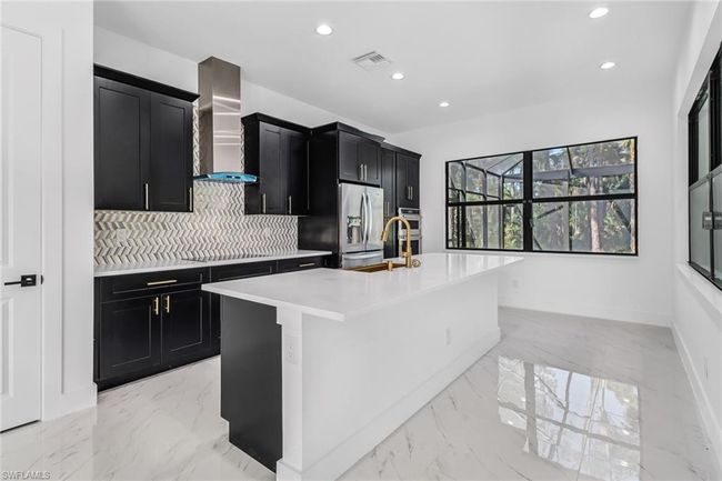 Kitchen with decorative backsplash, a center island with sink, wall chimney exhaust hood, and light tile patterned floors | Image 17