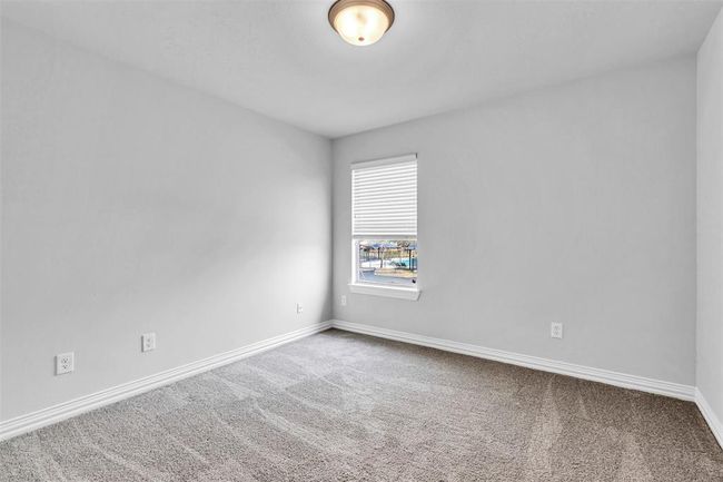 This photo shows a bright, carpeted room with neutral walls, a window with blinds, and a ceiling light, ideal for a cozy bedroom or office space. | Image 38