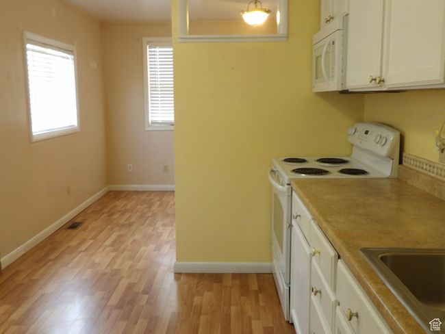 Kitchen featuring white appliances, white cabinetry, and light wood-type flooring | Image 20