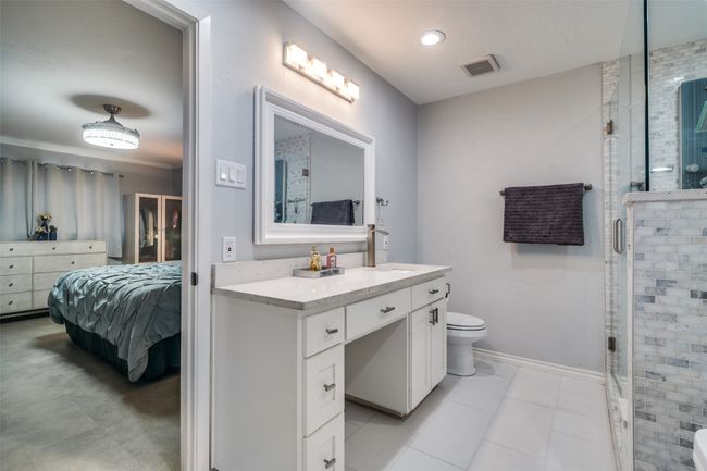 Ensuite bathroom with toilet, a stall shower, vanity, tile patterned floors, and baseboards | Image 12