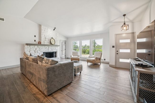 Living room featuring vaulted ceiling, recent tile floors, and a fireplace | Image 5