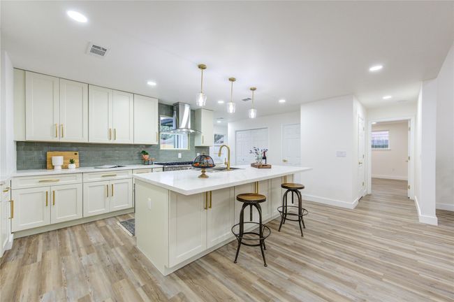 The island kitchen is a stunning focal point, fully renovated with Quartz countertops and a modern green subway tile backsplash that adds a pop of color. The spacious island provides ample counter space for meal prep and doubles as a casual dining area with seating. | Image 10