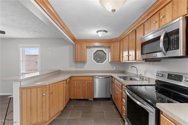 Kitchen with light countertops, stainless steel appliances, dark tile patterned flooring, a sink, and a peninsula | Image 10