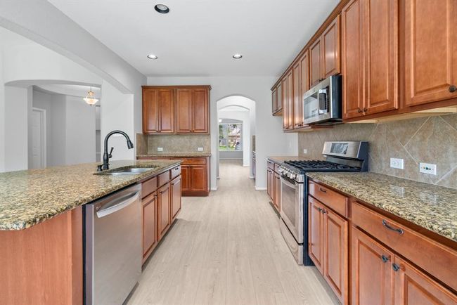 This modern kitchen is a chef’s dream, featuring clean lines, sleek cabinetry, and stainless steel appliances. Granite countertops, a large center island with bar seating, and contemporary lighting create a stylish and functional space. The open layout flows seamlessly into the living and dining areas, making it ideal for both everyday living and entertaining. | Image 11