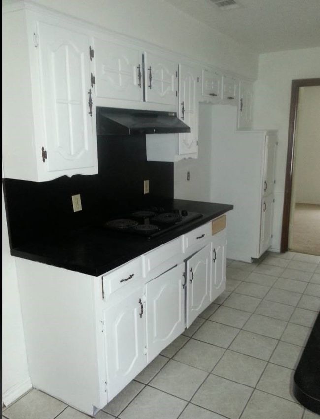 Kitchen with under cabinet range hood, dark countertops, white cabinets, and light tile patterned floors | Image 9