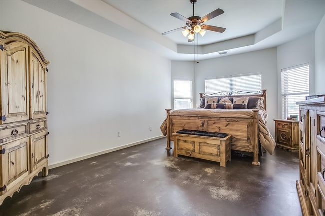 Primary bedroom with a ceiling fan, a raised ceiling, stained concrete floors, en-suite bathroom & a view of the back acreage. | Image 20
