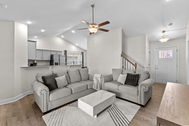 Living area with plenty of natural light, vaulted ceiling, light wood-type flooring, a ceiling fan, and stairway | Image 13