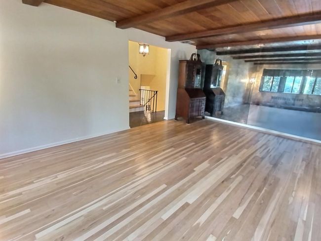 Unfurnished living room with wood ceiling with exposed beams, wood finished floors, and stairway | Image 10
