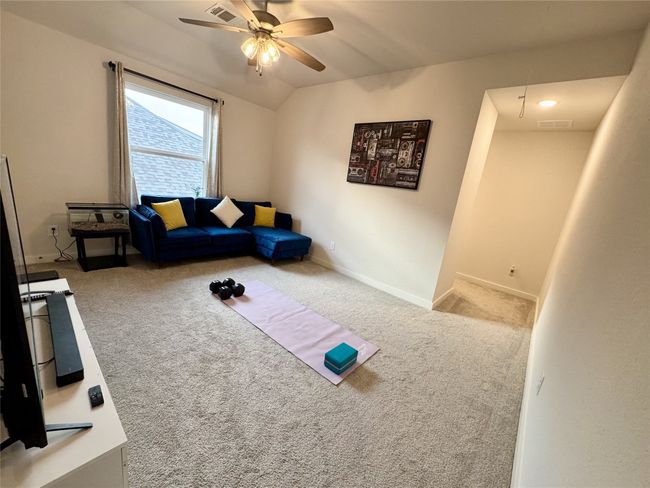 Carpeted living area featuring ceiling fan, vaulted ceiling, baseboards, and attic access | Image 9