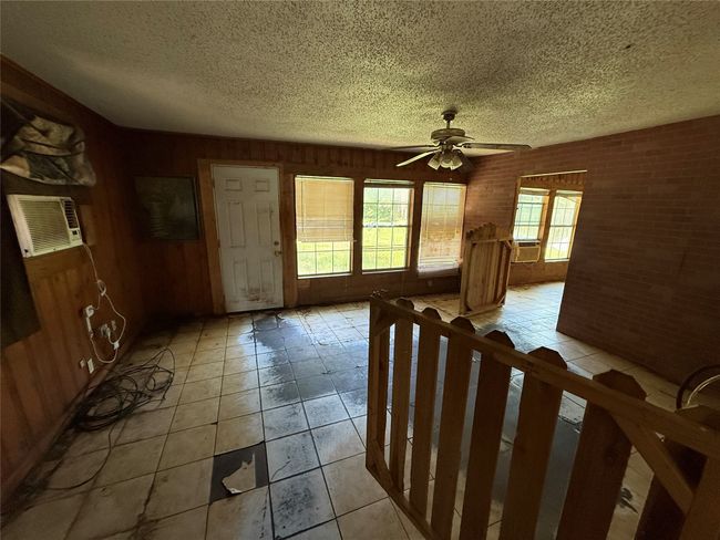 Foyer featuring a textured ceiling, a ceiling fan, brick wall, light tile patterned floors, and cooling unit | Image 9