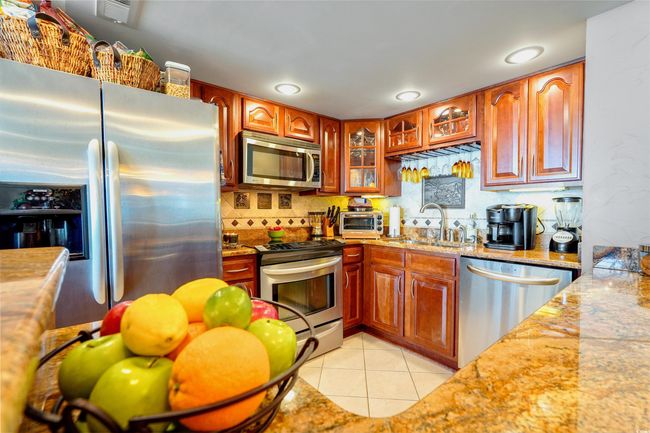 Kitchen with stainless steel appliances, a sink, light tile patterned floors, glass insert cabinets, and decorative backsplash | Image 15
