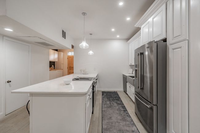 Kitchen with stainless steel appliances, a peninsula, light wood-style flooring, visible vents, and light countertops | Image 20
