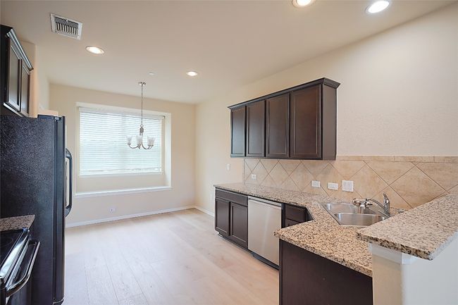 Kitchen with a chandelier, dark brown cabinets, stainless steel dishwasher, light stone counters, and black / electric stove | Image 6