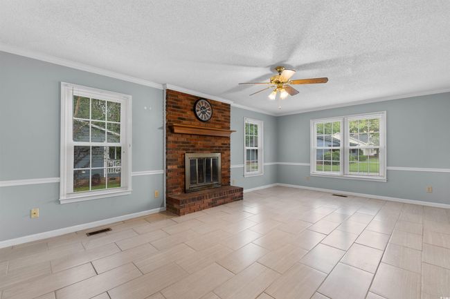 Unfurnished living room with ceiling fan, a textured ceiling, a brick fireplace, and ornamental molding | Image 13