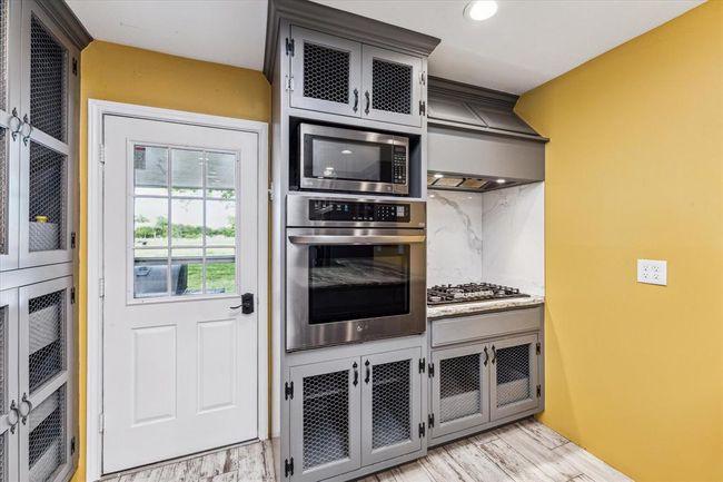 Another view of the kitchen showing access to the back patio, black stainless appliances, propane cooktop, and more cabinets | Image 18