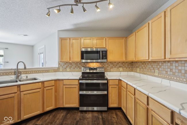 kitchen featuring stainless steel appliances, a sink, light brown cabinetry, a textured ceiling, and dark wood-style flooring | Image 27