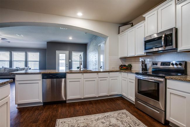 Kitchen with white cabinetry, tasteful backsplash, kitchen peninsula, dark wood-type flooring, and stainless steel appliances | Image 9