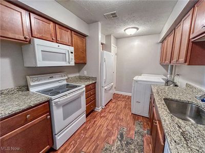 Kitchen with granite countertops, sink, white appliances, laundry area, and a textured ceiling. | Image 2