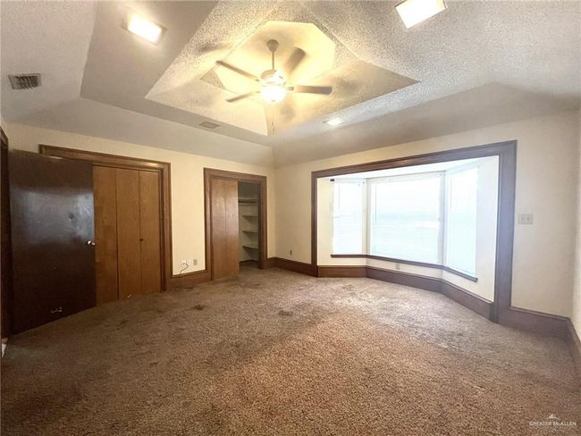 Unfurnished bedroom with a raised ceiling, a textured ceiling, light carpet, multiple closets, and ceiling fan | Image 10