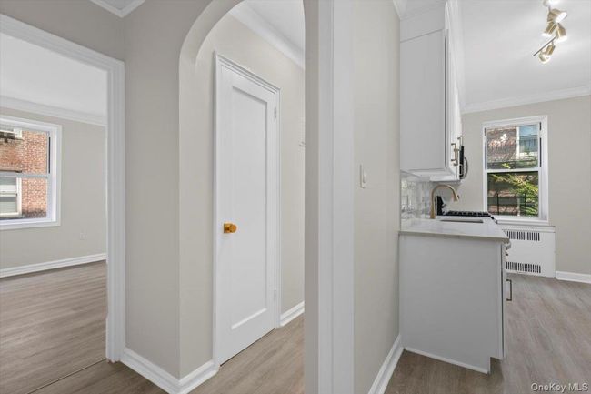 Hall with crown molding, light wood-style flooring, arched walkways, and radiator | Image 8