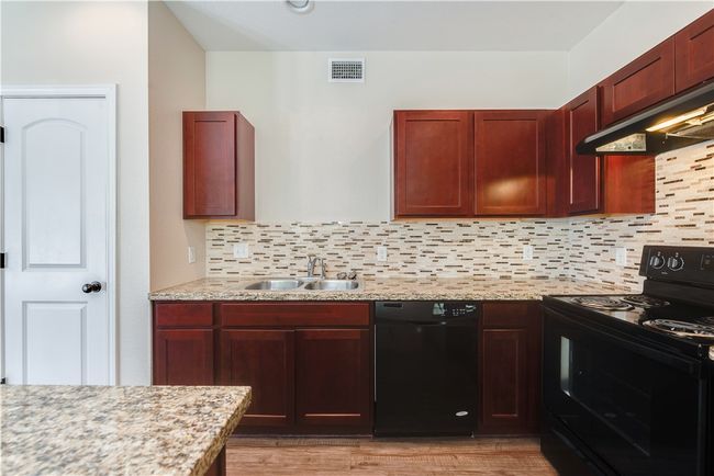 Kitchen with black appliances, decorative backsplash, range hood, and visible vents | Image 4