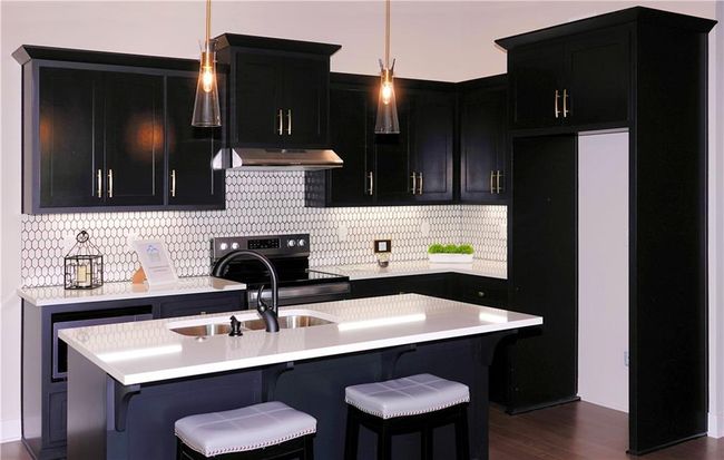 Kitchen featuring light countertops, an island with sink, under cabinet range hood, and dark cabinets | Image 18