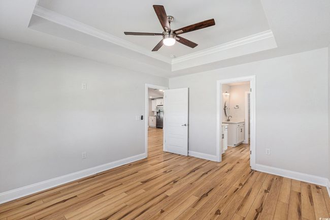 Unfurnished bedroom featuring a raised ceiling, stainless steel fridge, ornamental molding, light wood-style flooring, and connected bathroom | Image 16