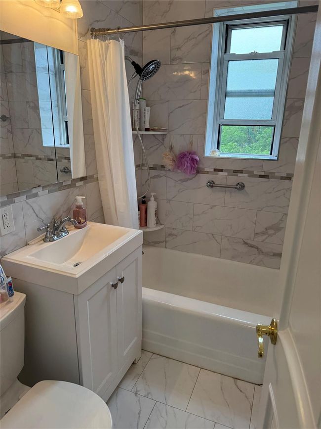Full bath featuring toilet, shower / bath combo, vanity, marble look tiles, and tile walls | Image 10