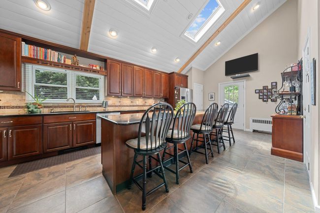 Kitchen featuring stainless steel appliances, dark countertops, beamed ceiling, a kitchen island, and a kitchen breakfast bar | Image 17