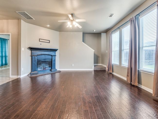 Unfurnished living room with visible vents, hardwood / wood-style flooring, a ceiling fan, and a glass covered fireplace | Image 4