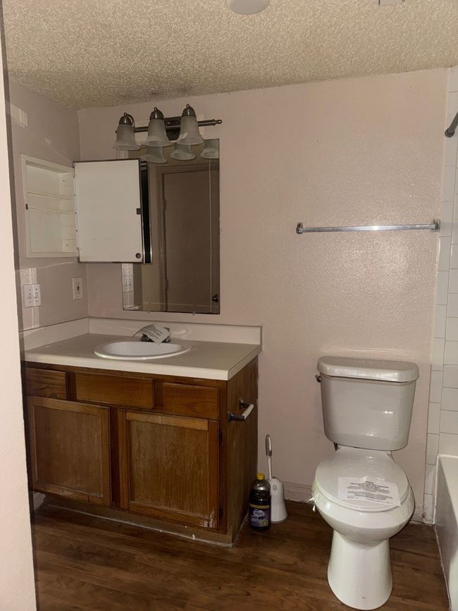 Full bath with a textured ceiling, dark wood-type flooring, vanity, and shower / bath combination | Image 10