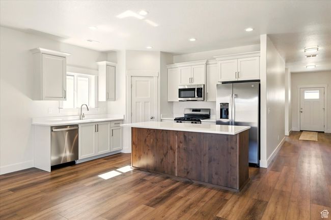 Kitchen with stainless steel appliances, white cabinetry, dark wood-style flooring, light countertops, and baseboards | Image 9