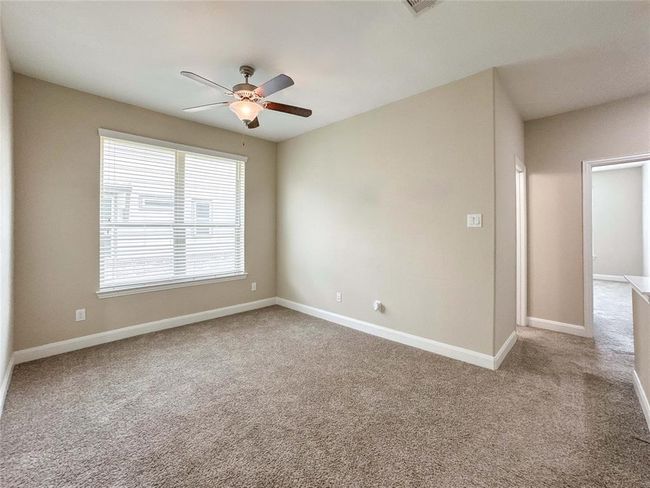 Enjoy this bright, spacious game room located on the second floor, with neutral walls and carpeted flooring. It features a ceiling fan and a large window offering natural light. There is an adjoining hallway leading to the secondary bedrooms. | Image 13