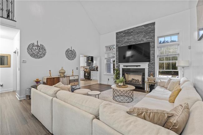 Living area with high vaulted ceiling, wood finished floors, baseboards, and a fireplace | Image 4