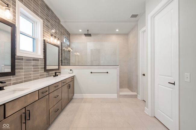 Primary bathroom rich in detail with walk in tiled shower, decorative backsplash, beautiful cabinetry, double vanity, and large closet. | Image 19