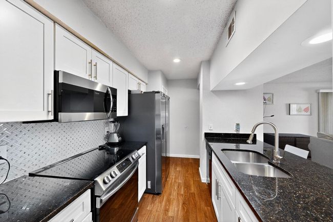Kitchen featuring stainless steel appliances, white cabinets, tasteful backsplash, dark stone counters, and a textured ceiling | Image 9