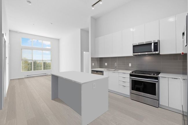 Kitchen with light wood finished floors, a center island, a sink, baseboard heating, and appliances with stainless steel finishes | Image 12